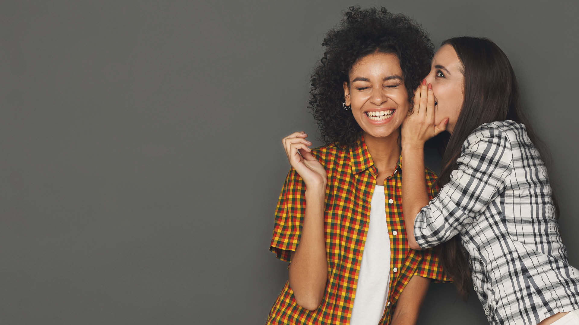 Jeune femme chuchotant à l'oreille d'une autre femme en plein fou rire