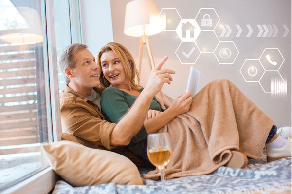 Couple dans un lit, sou sun plaid, avec des signes numérique autour d'eux pour symboliser la maison connectée
