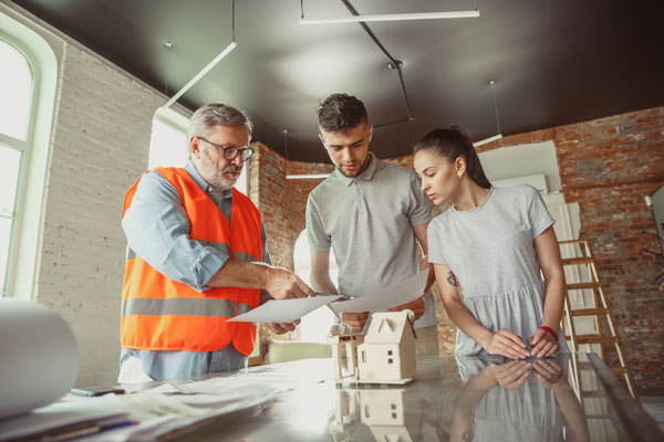 Un constructeur de maison présentant des plans à un jeune couple