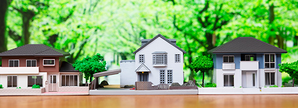 Trois maquettes de maisons posées sur une table avec en arrière plan de la verdure