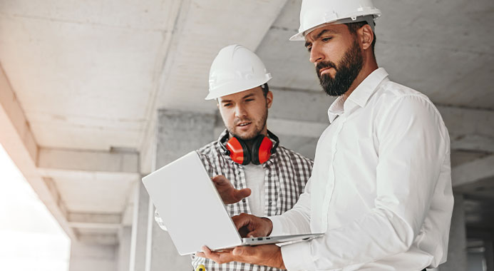 Constructeur maison avec ouvrier devant ordinateur ouvert