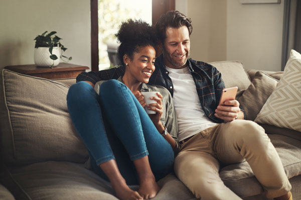 Jeune couple sourires dans un canapé salon devant un téléphone