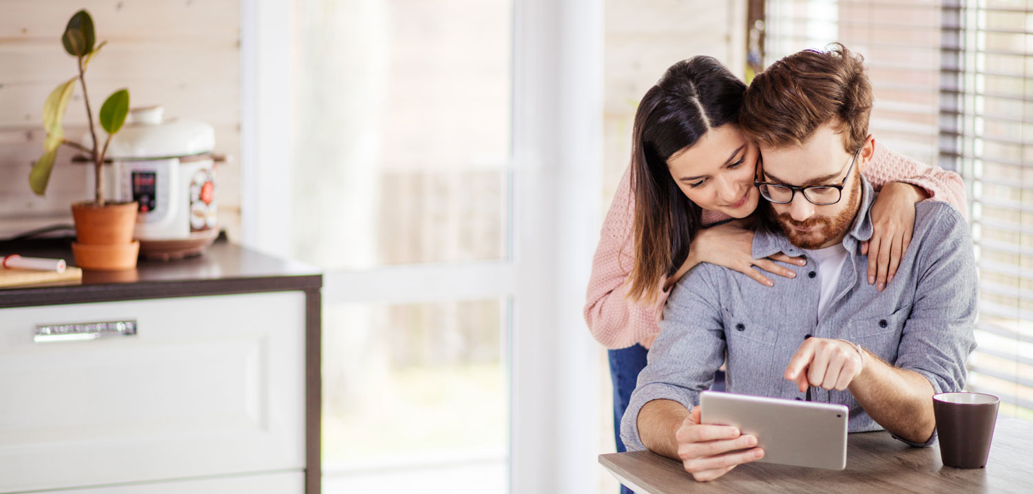 Couple heureux dans leur cuisine devant leur tablette