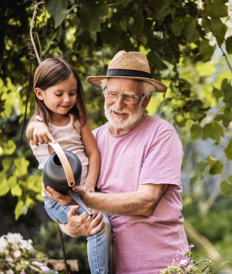 Grand père dans son jardin avec sa petite fille tenant un arrosoir
