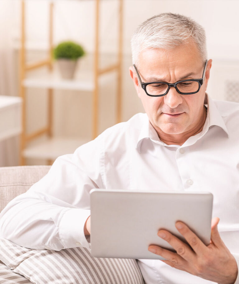Senior en retraite devant une tablette assis sur un canapé